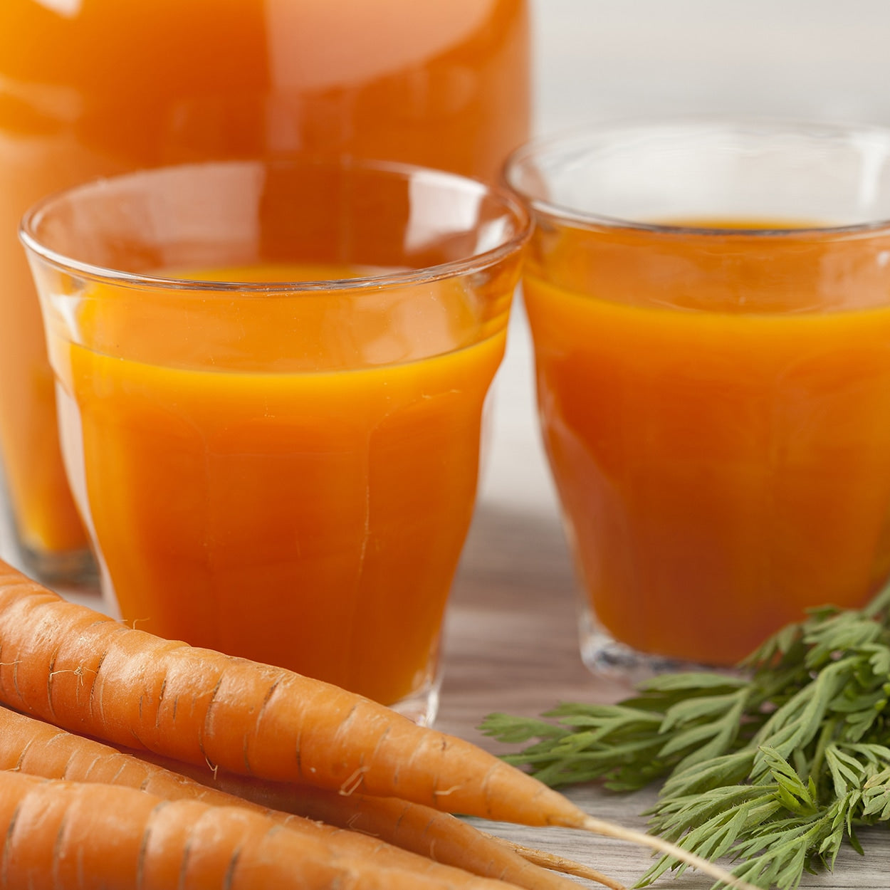 Carrots on a  counter with carrot juice next to it 